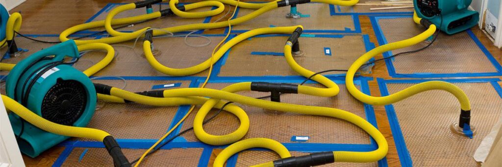 A floor drying system with yellow hoses and air movers actively restoring water damage at AdvantaClean of Cabarrus and Rowan Counties in Concord, NC.