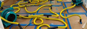 A floor drying system with yellow hoses and air movers actively restoring water damage at AdvantaClean of Cabarrus and Rowan Counties in Concord, NC.