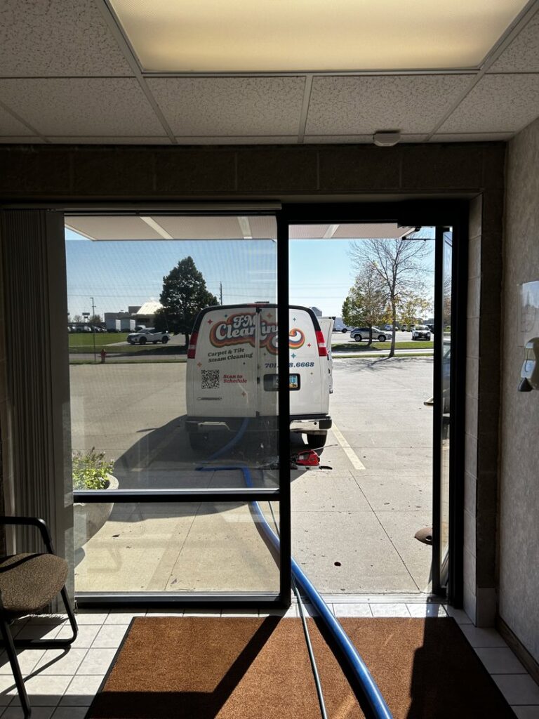 The FM Cleaning van parked outside a commercial building with a cleaning hose extended inside in West Fargo, ND.