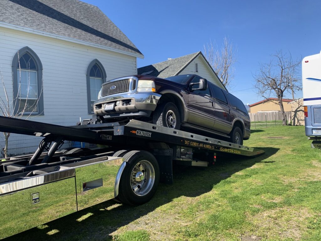 A maroon Ford Excursion SUV is loaded onto a flatbed tow truck by S&F Towing in Oakland, CA.