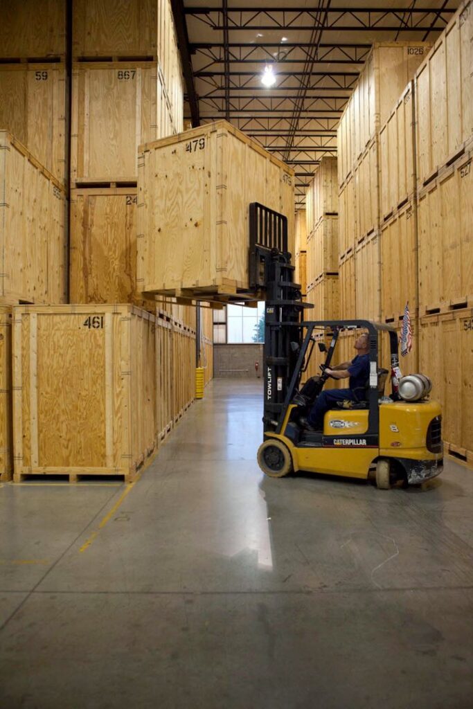 A forklift moving a large wooden storage crate in the warehouse of Leaders Moving & Storage Co. in Indianapolis, IN.