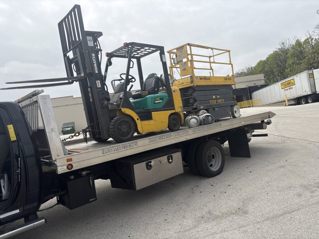 A forklift and a scissor lift being transported on a flatbed tow truck by Towing Recovery Rebuilding Assistance Services in Naperville, IL