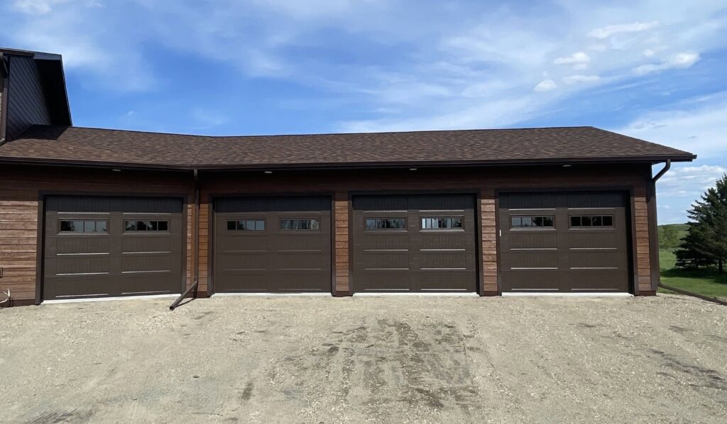 Four brown garage doors with windows on a residential property, installed by PS GARAGE DOORS in Grand Forks, ND