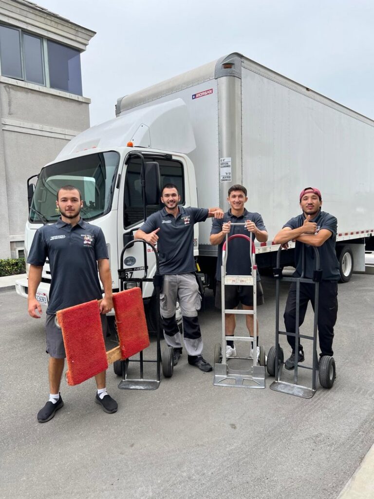 Four professional movers with dollies and moving pads standing in front of a large moving truck for All Way Moving in Washington, PA.