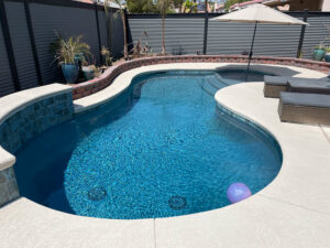 A beautiful freeform pool with a small waterfall feature and surrounding patio by Steve Breck Pools in Las Vegas, NV.