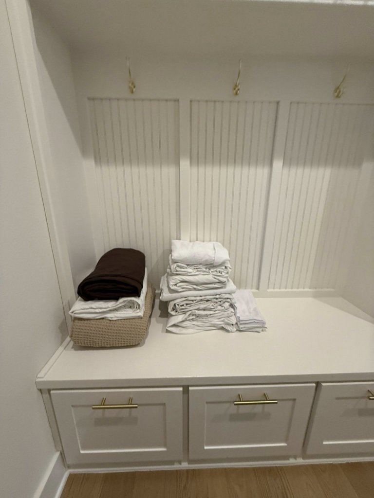 Freshly folded laundry, including towels and sheets, neatly stacked on a bench by Global Provisions, AR in Fayetteville, AR.