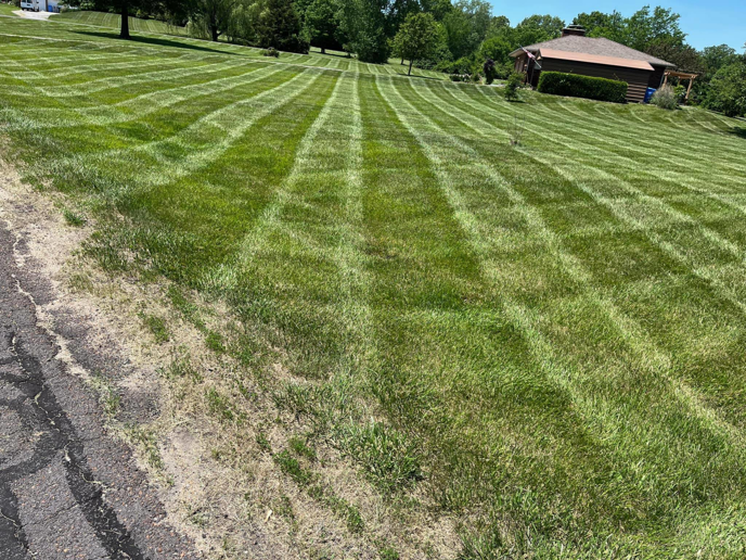 A large, freshly mowed lawn with distinct stripes, showcasing professional lawn care by Kemple Lawn Care in Lawrence, KS.