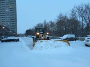A front-end loader with a plow blade clearing snow in a parking lot, providing snow removal services for JC Snow Management in Mount Vernon, NY
