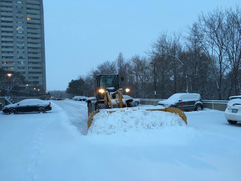 A front-end loader with a plow blade clearing snow in a parking lot, providing snow removal services for JC Snow Management in Mount Vernon, NY