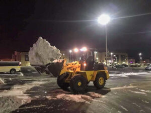 A front-end loader moving a large pile of snow in a parking lot at night by ASAP Mow & Snow, LLC in Toledo, OH