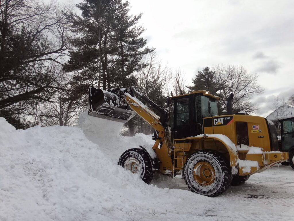 A yellow front-end loader efficiently moving a large pile of snow, demonstrating snow removal by The Groundskeeper Inc. in Fort Collins, CO.