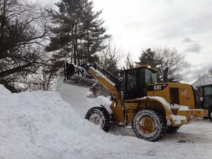 A yellow front-end loader efficiently moving a large pile of snow, demonstrating snow removal by The Groundskeeper Inc. in Fort Collins, CO.