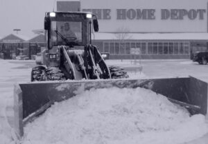 A front-end loader with a plow blade clearing snow in front of a Home Depot store for JC Snow Management in Mount Vernon, NY