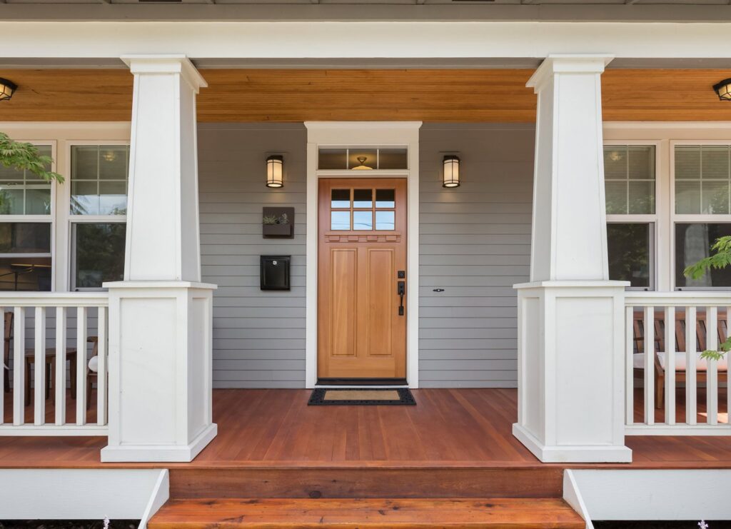 A welcoming front porch of a house with light grey horizontal siding and a natural wood door, by Jonesboro Siding, Window & Door in Jonesboro, AR.