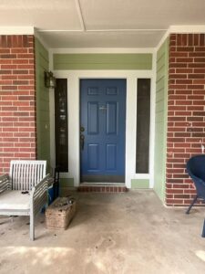 A welcoming front porch featuring light green siding and brick columns, a project by Ideal Siding Austin in Austin, TX.