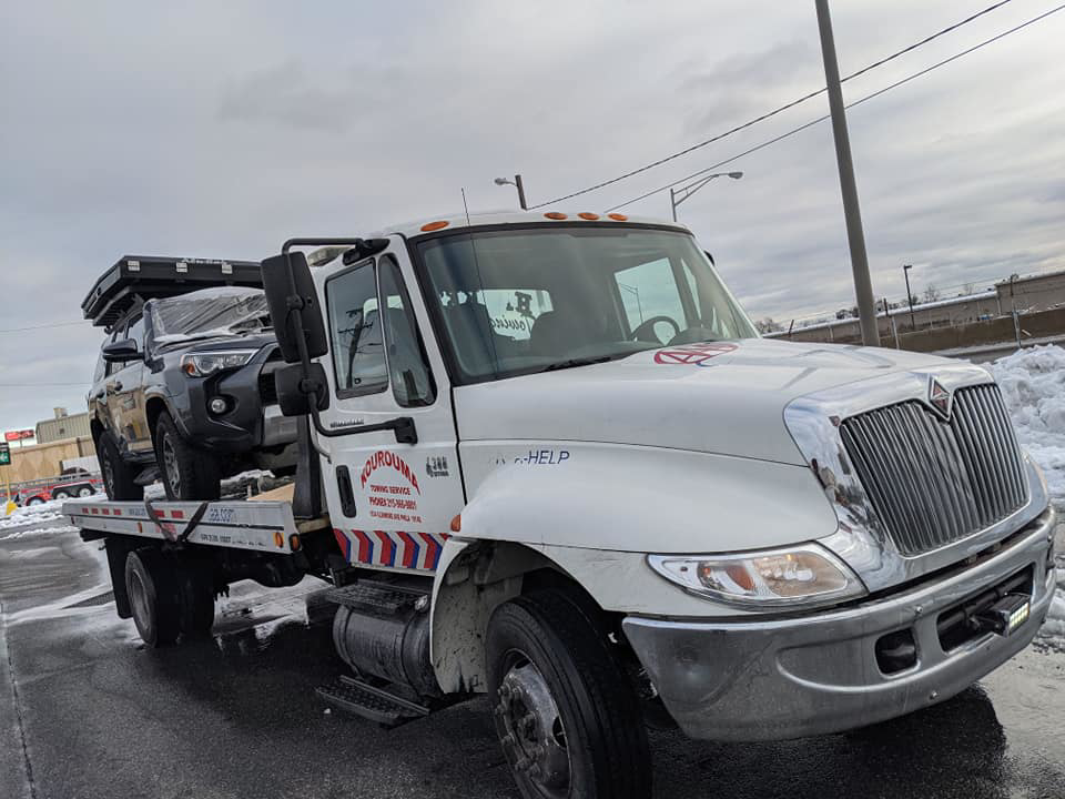 A Kourouma Towing Services flatbed tow truck transporting a dark grey SUV on a snowy day in Philadelphia, PA.
