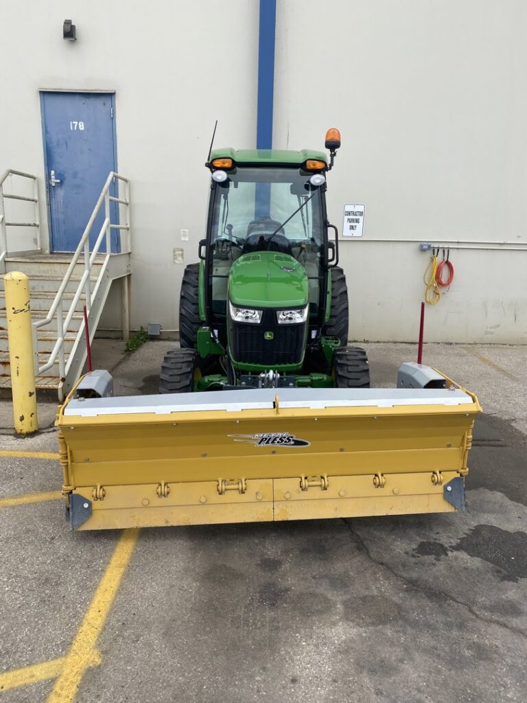 Front view of a John Deere tractor with a yellow snow plow attachment, used by Turf Pro Lawn Care & Snow Removal in Green Bay, WI.