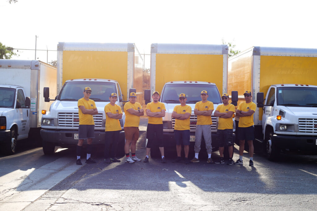 The full team of movers from Sunshine Moving Services LLC posing with their fleet of moving trucks in San Diego, CA.