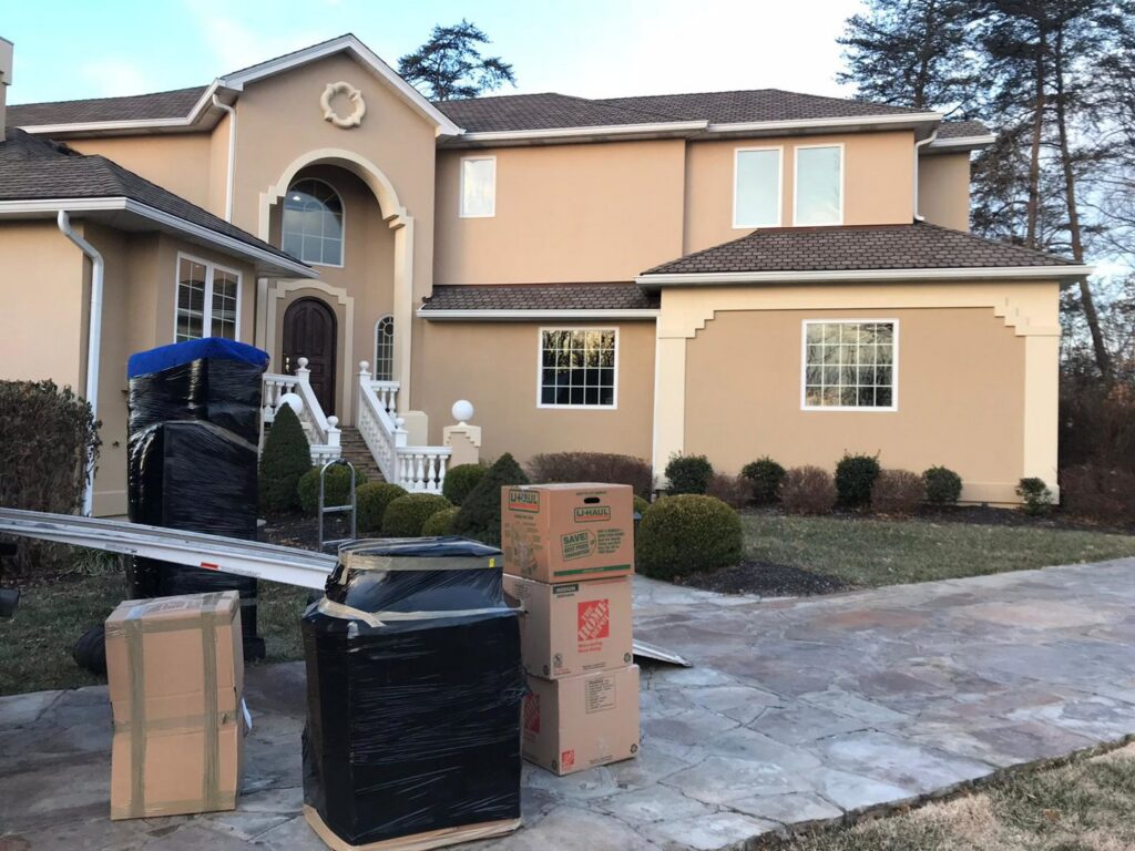 Wrapped furniture and moving boxes are placed on the driveway outside a large house by J.Gentle Van Lines in Elizabeth, NJ.