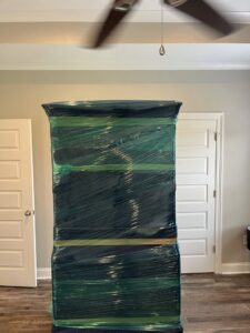 A tall piece of furniture meticulously wrapped in protective plastic for moving by Gifted Journey Movers in Gulfport, MS.