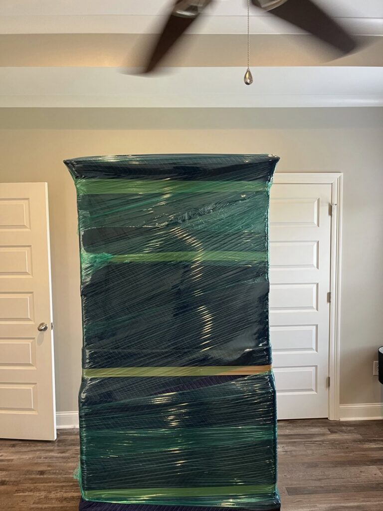 A tall piece of furniture meticulously wrapped in protective plastic for moving by Gifted Journey Movers in Gulfport, MS.
