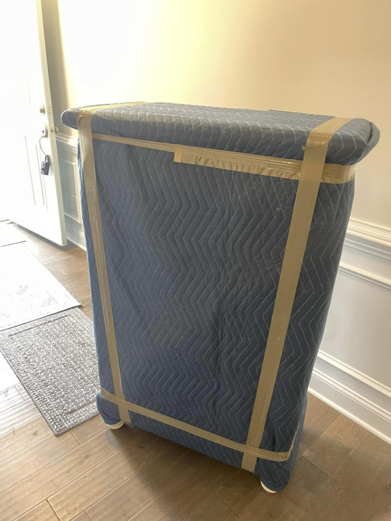 A piece of furniture wrapped in a blue moving blanket and tape, ready for transport by CNZ Moving in Raleigh, NC.