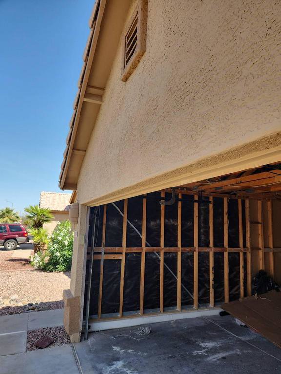Garage interior with exposed studs and black sheeting, indicating demolition work after water damage by Lotus Restoration Services in Gilbert, AZ.