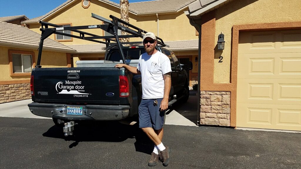A Garage Door Mesquite contractor standing next to a branded truck in Mesquite, NV, with a residential garage door in the background.