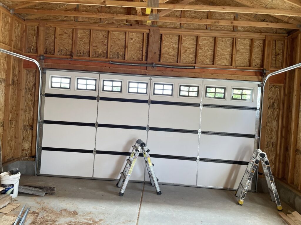 Interior view of a garage with a white door and two ladders, indicating a garage door installation in progress by Delta Garage Door in Millcreek, UT.
