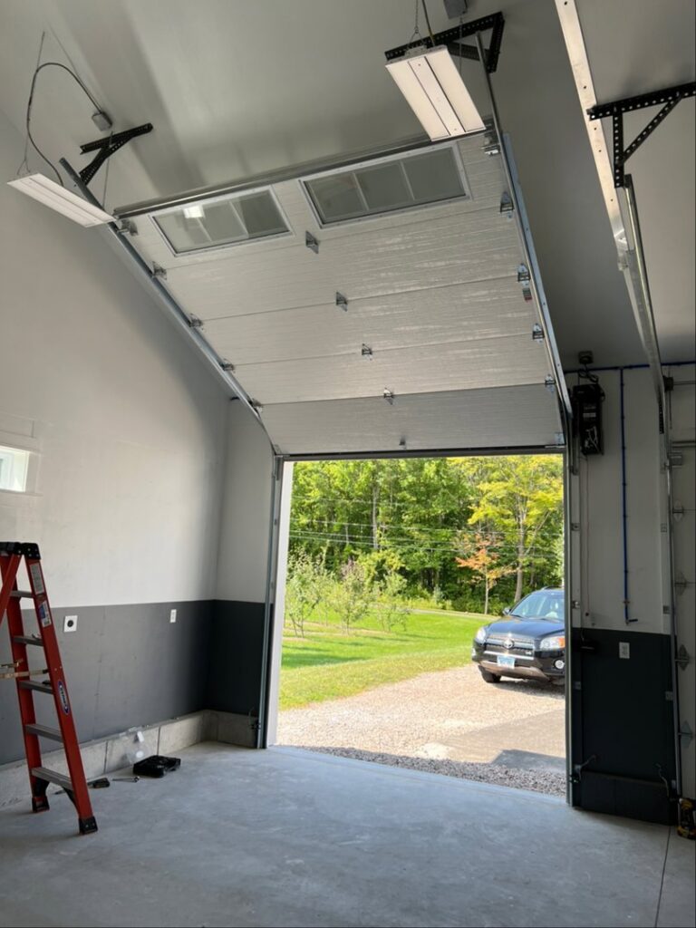 Interior view of a garage with a white sectional door partially open, showing a new installation by Douglas Garage Door Center in East Hartford, CT.