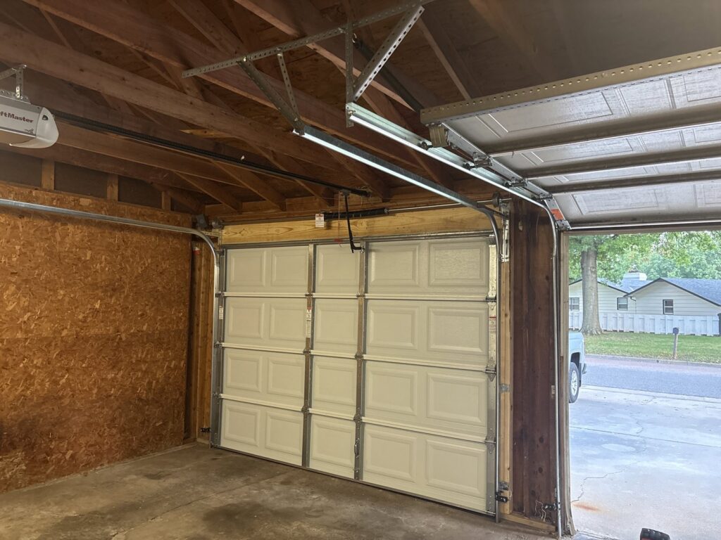 Interior view of a garage showing a newly installed white panel door and opener mechanism by The Door Pros in Wichita, KS