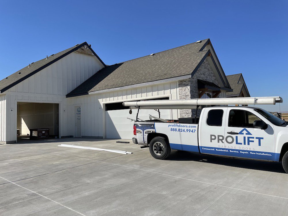 A ProLift Garage Doors of Canyon County truck at a new construction site, installing a white garage door in Nampa, ID.