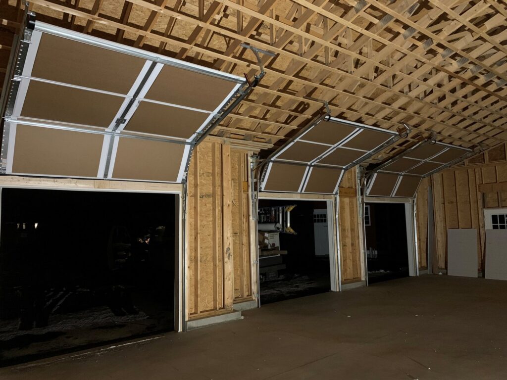 Interior view of a garage showing three garage doors partially open with tracks and mechanisms by J.A. Overhead Door in Westfield, MA.