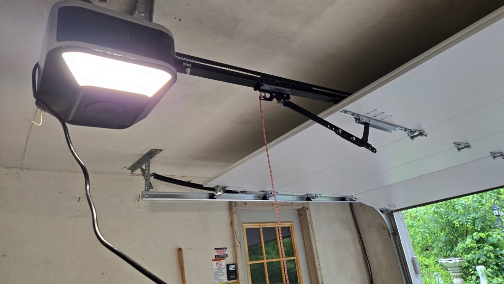 A LiftMaster garage door opener and top panel of a garage door, showing installation by The Garage Door Guys, LLC in New Haven, CT.
