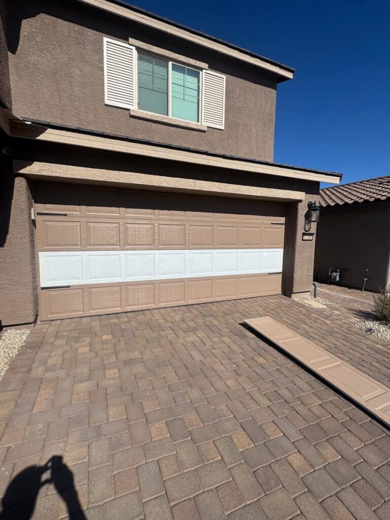 A garage door with new white panels installed, showing a repair or replacement job by Lifetime Garage Door in Las Vegas, NV.