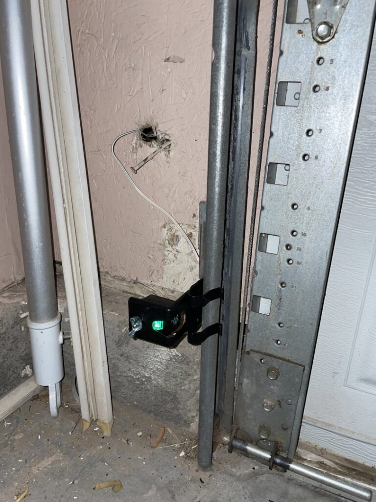 A close-up view of a garage door safety sensor, indicating installation or repair work by Lifetime Garage Door in Las Vegas, NV.