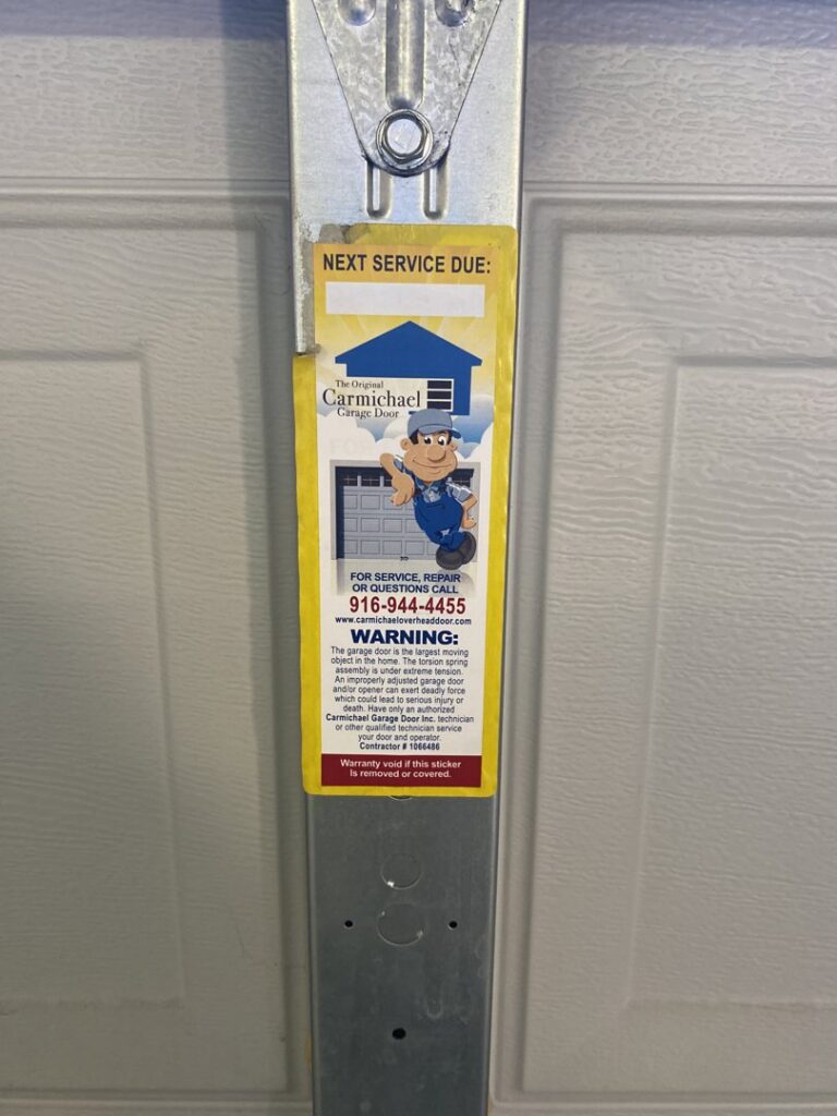 A service sticker from Carmichael Garage Door on a garage door track, indicating maintenance or repair work in Carmichael, CA.
