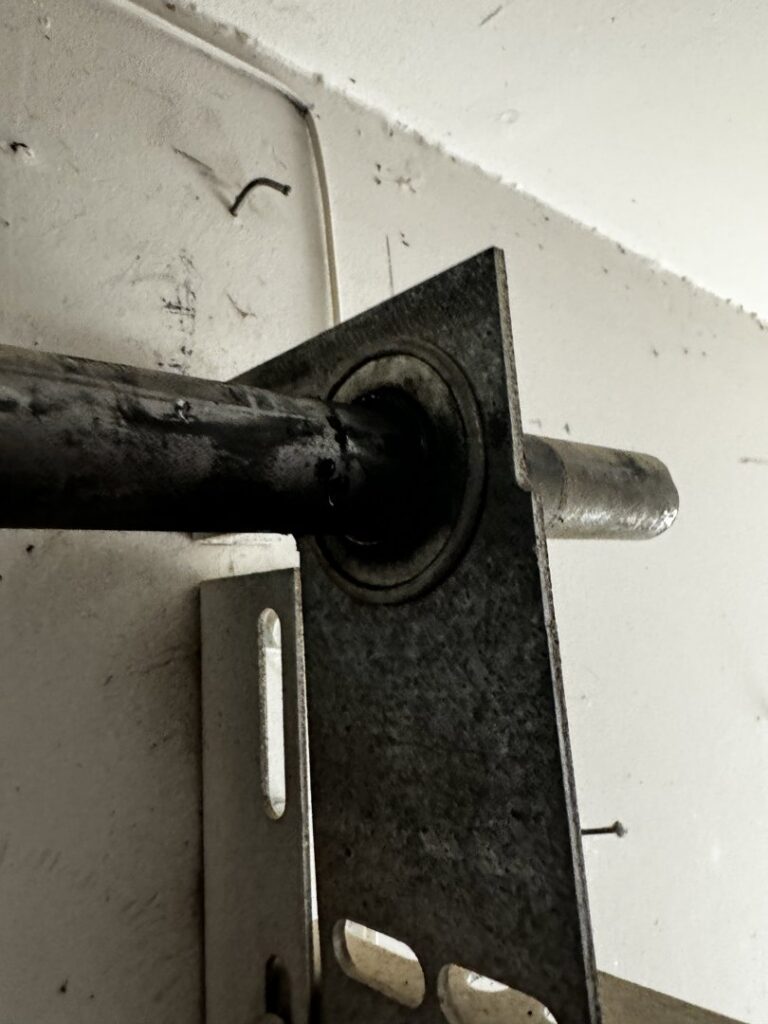 A close-up view of a garage door shaft and bearing plate, indicating repair or installation by Apex Garage Doors LLC in Las Vegas, NV