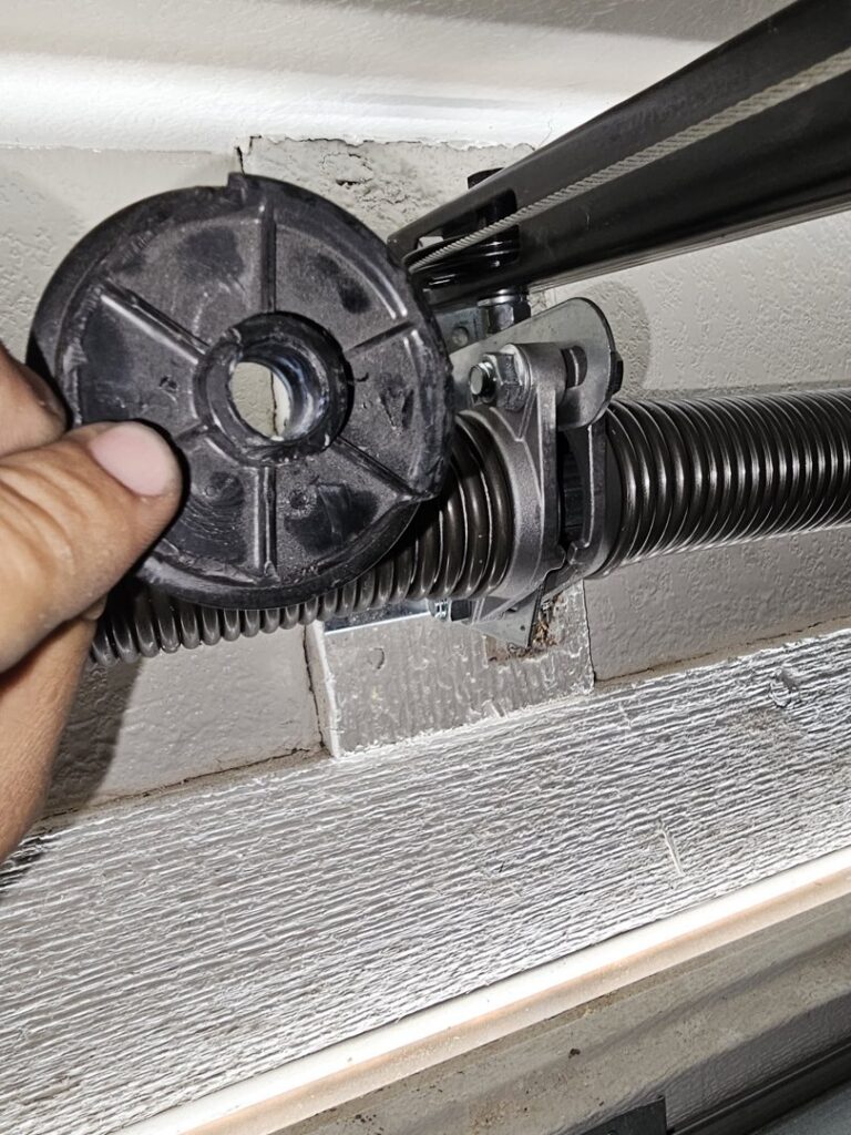 A close-up of a technician's hand holding a garage door cable drum during a torsion spring repair by Rebel Overhead Doors in Las Vegas, NV.