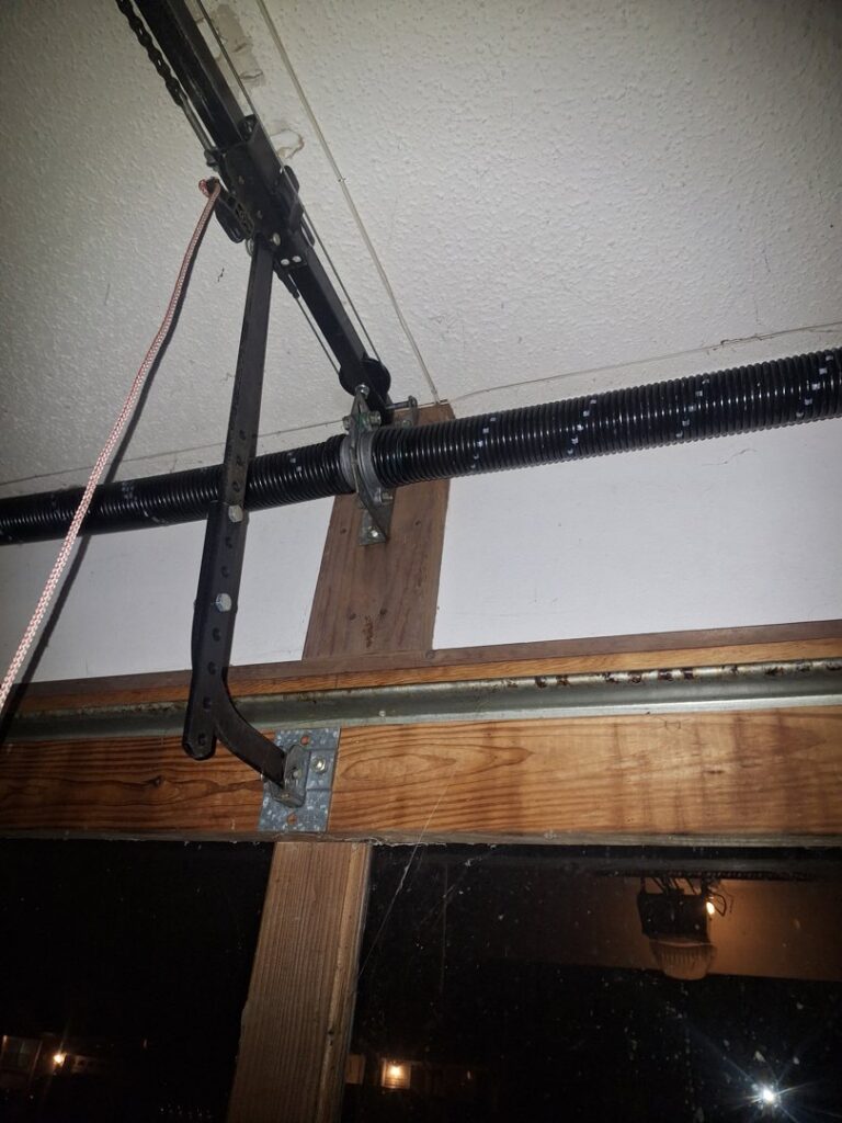 Close-up view of a garage door torsion spring system and track, indicating repair or maintenance by LaFrancis Overhead Door LLC in Little Rock, AR