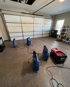 Water damage drying equipment, including air movers and a dehumidifier, set up in a garage by Sentry Restoration in Volo, IL