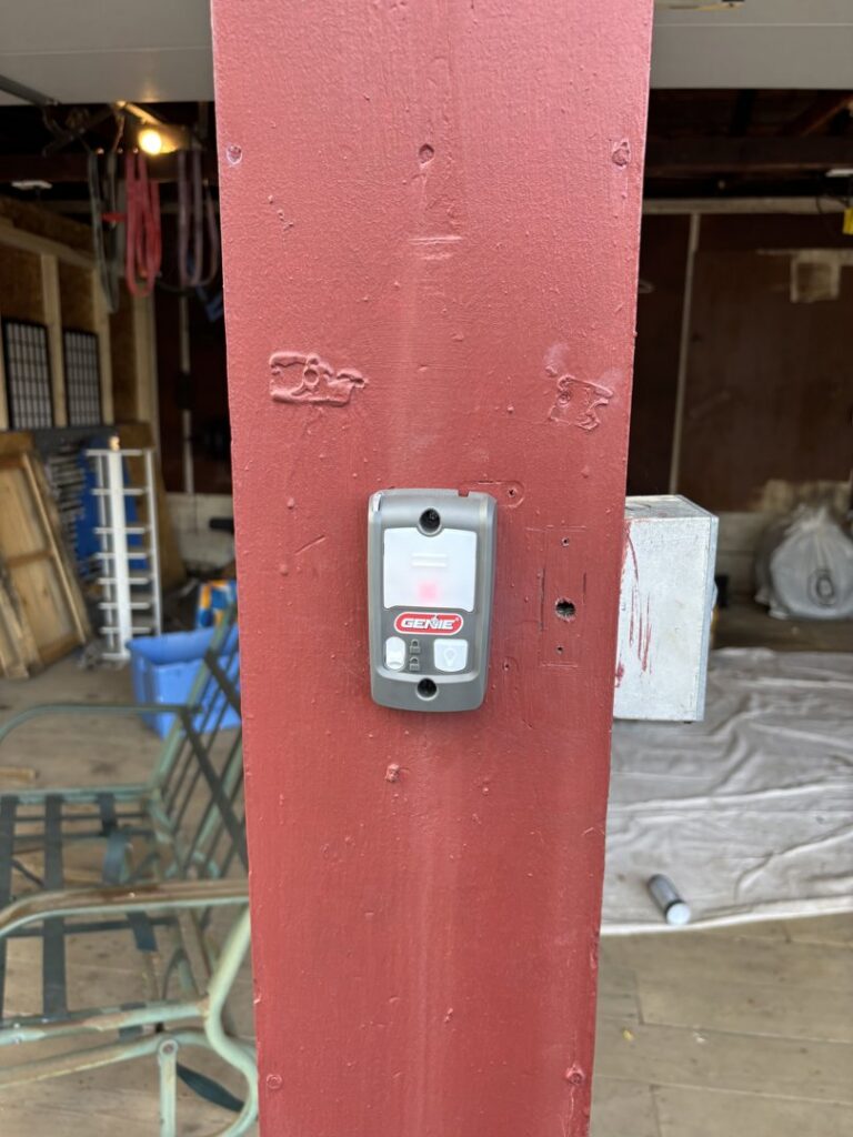 A Genie garage door opener button installed on a red post by Precision Garage Door Service of NC in Morrisville, NC.