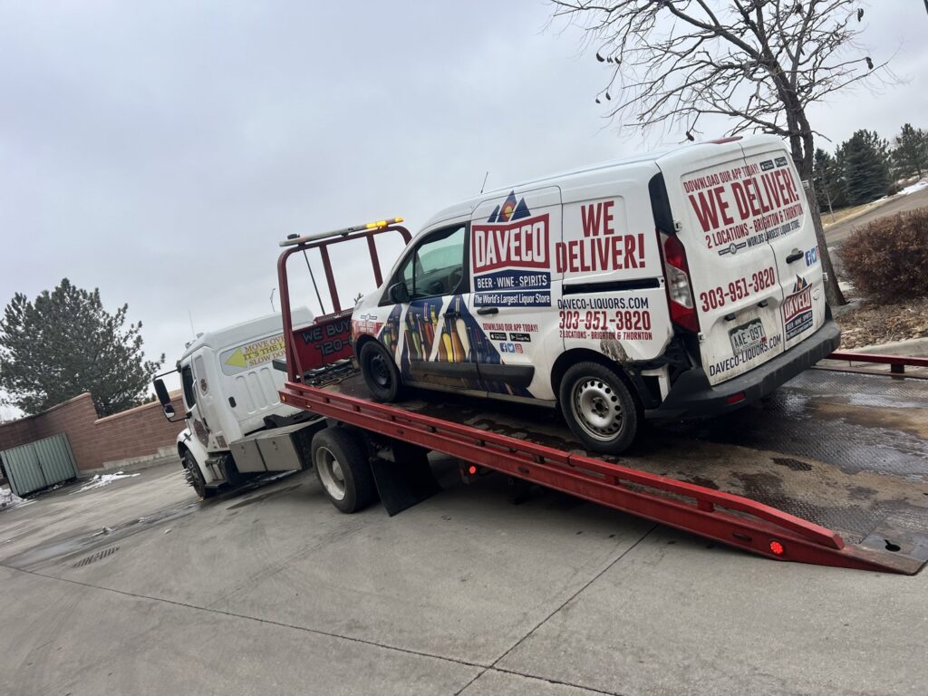Giner's Towing flatbed truck transporting a white delivery van in Aurora, CO.