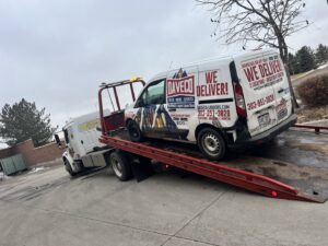 Giner's Towing flatbed truck transporting a white delivery van in Aurora, CO.