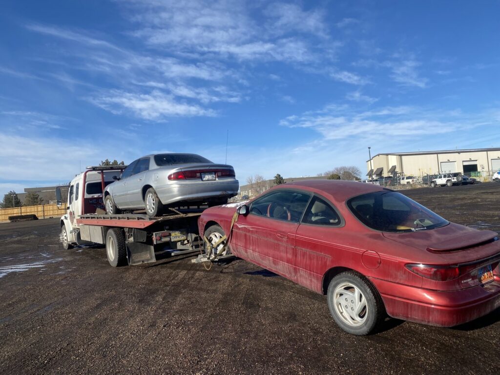 Giner's Towing performing a double tow with a silver sedan on the flatbed and a red coupe in Aurora, CO.