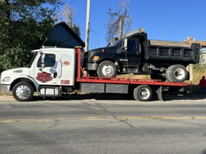 Giner's Towing flatbed truck transporting a black dump truck in Aurora, CO.