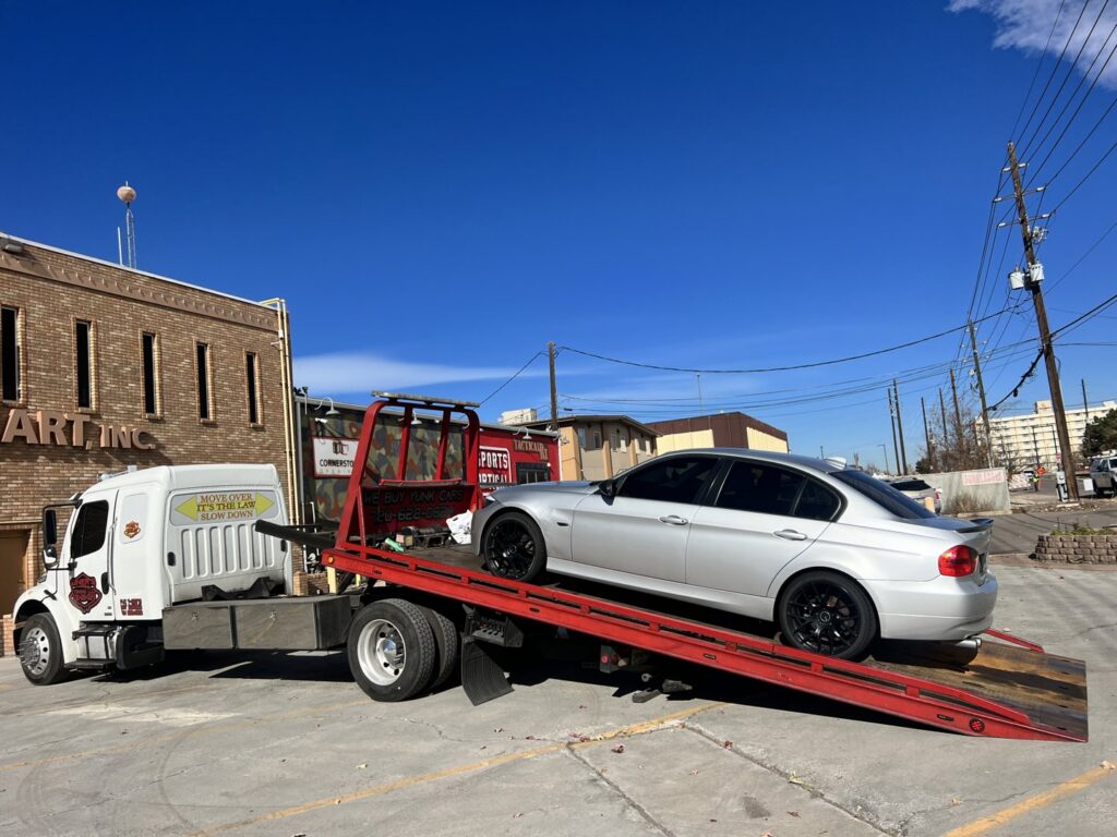Giner's Towing flatbed truck loading a silver sedan for transport in Aurora, CO.