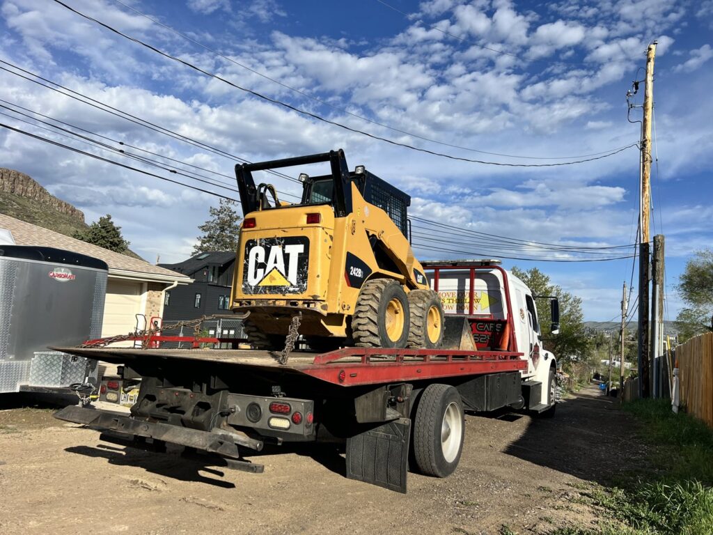 Giner's Towing flatbed truck transporting a yellow CAT skid steer loader in Aurora, CO.