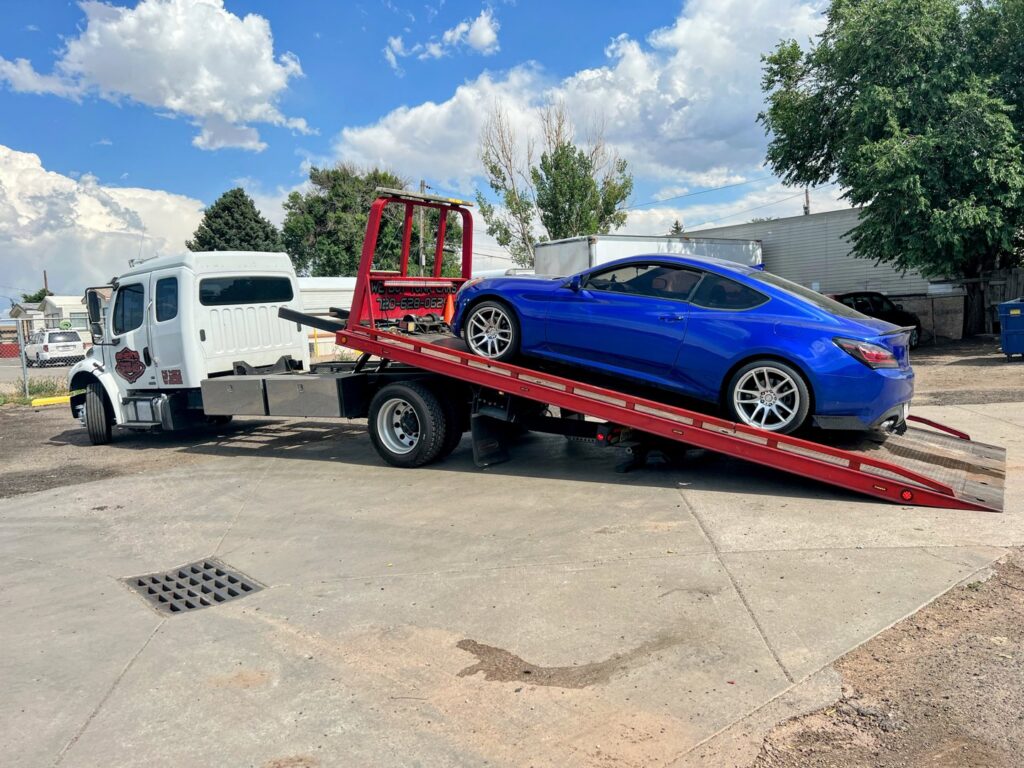 Giner's Towing flatbed truck transporting a blue sports car in Aurora, CO.