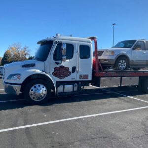 A Giner's Towing flatbed truck transporting a white SUV during the daytime in Aurora, CO.